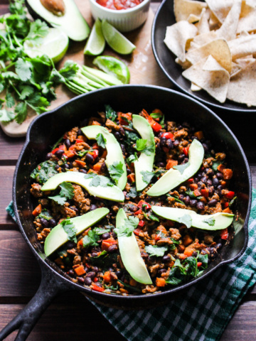 skillet with colorful vegetables, beans, turkey, and decorative slices of avocado with chips, salsa, and cilantro