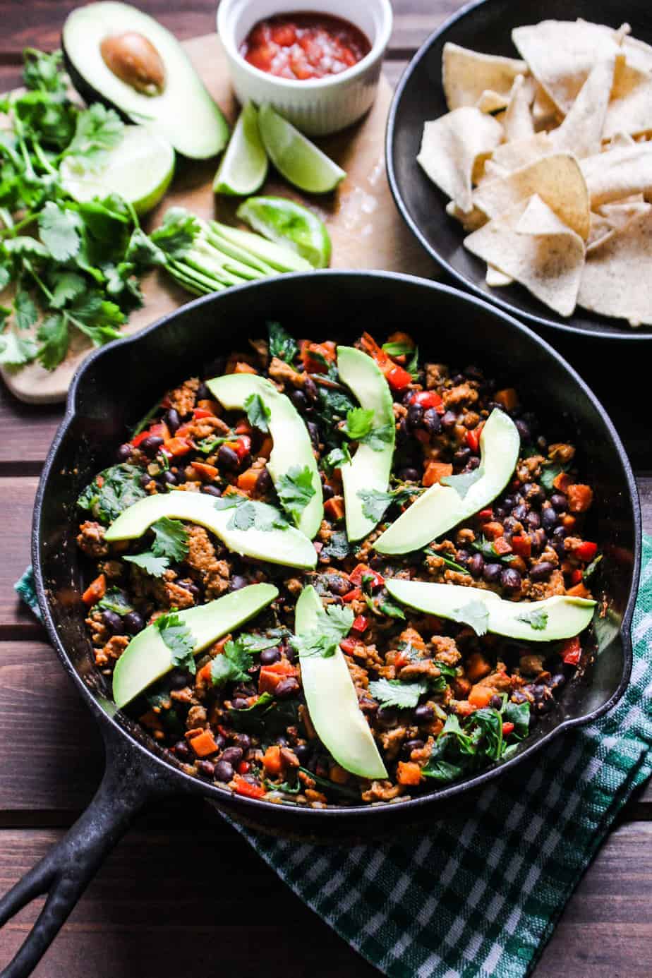 skillet with colorful vegetables, beans, turkey, and decorative slices of avocado with chips, salsa, and cilantro