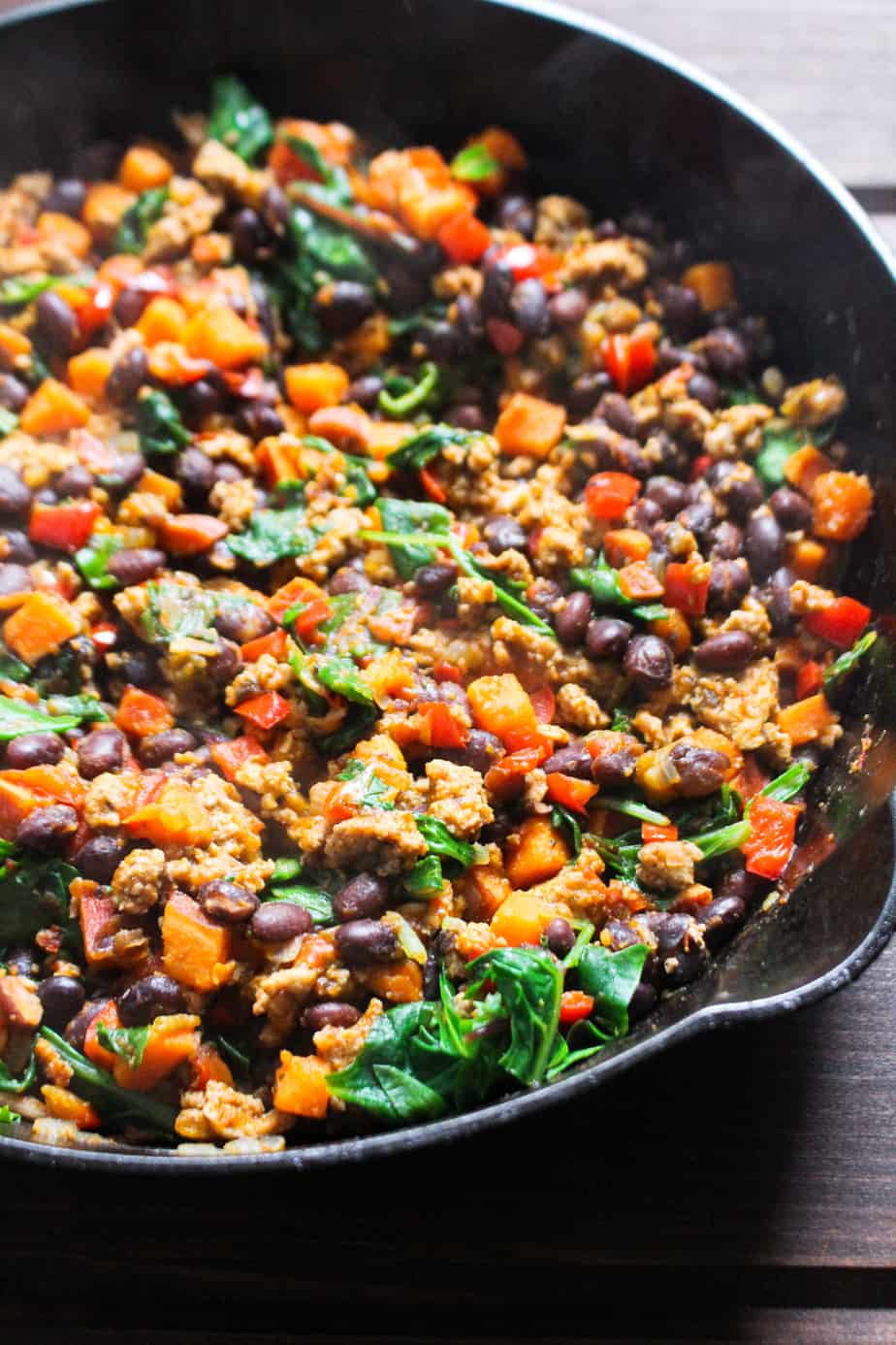 Cast iron skillet with cooked ground turkey, colorful vegetables and black beans.