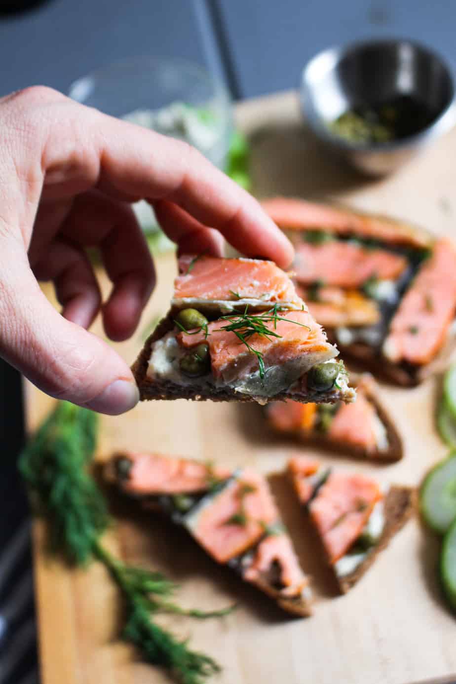 hand holding a triangle of pumperknickel smoked salmon toast