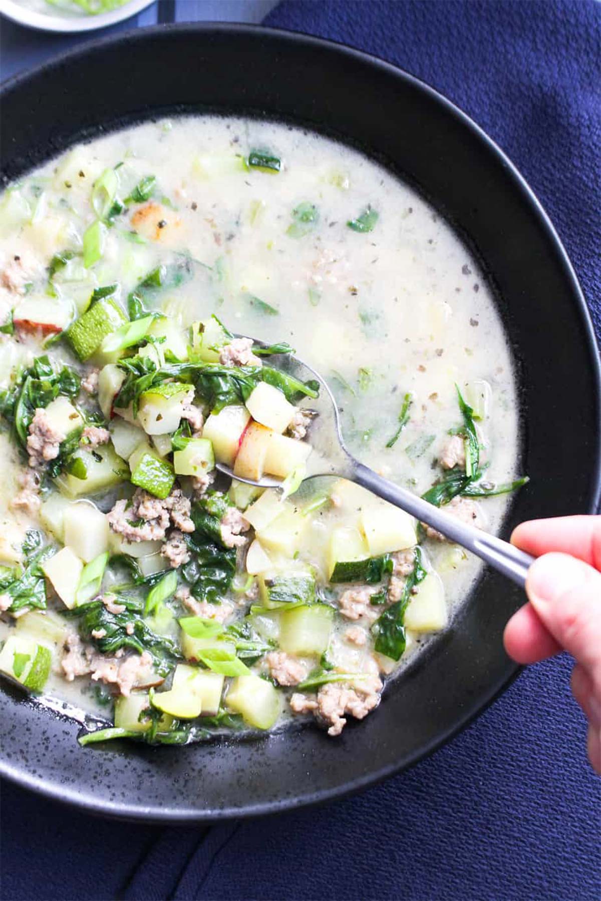 A bowl of pork soup on the table with a hand reaching in to pick up a bite.