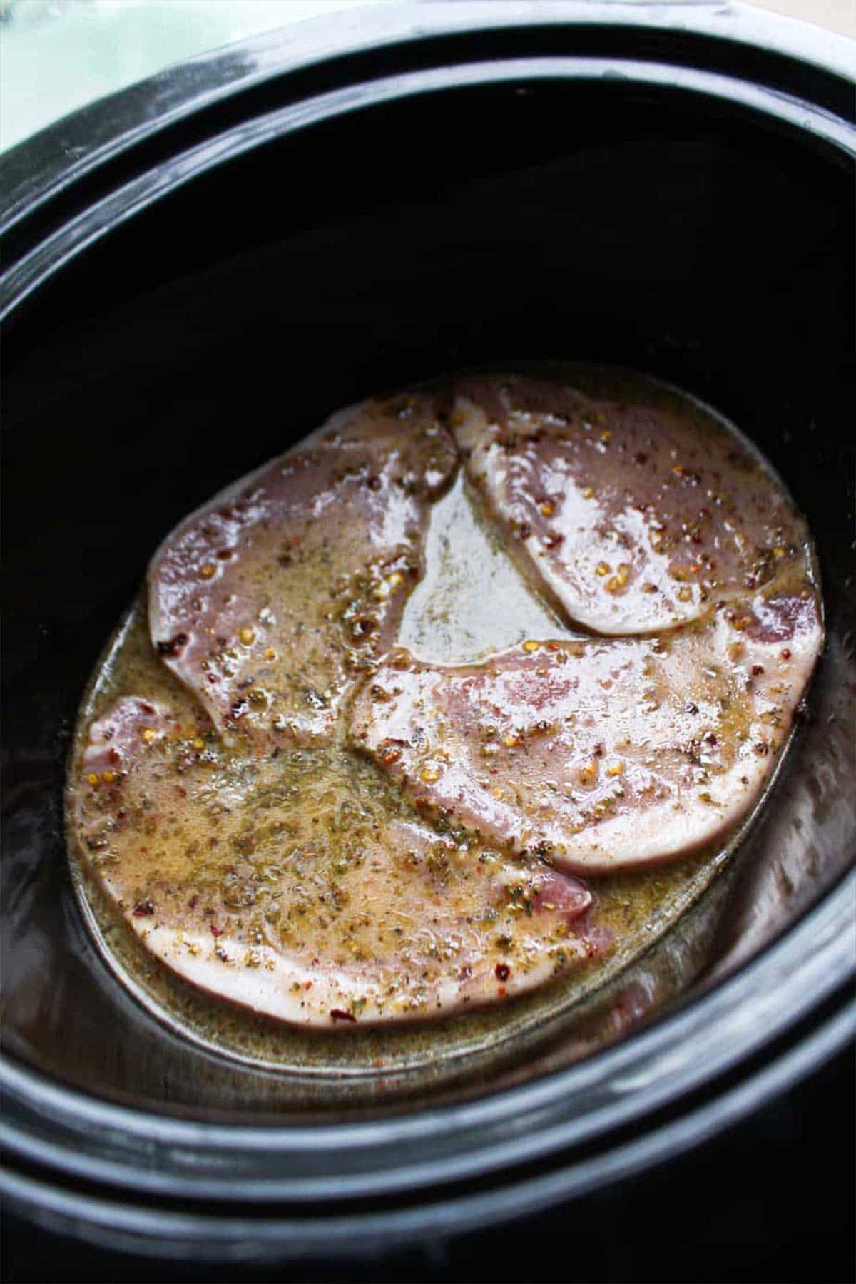 Pork chops and marinade layered on the bottom of the slow cooker.