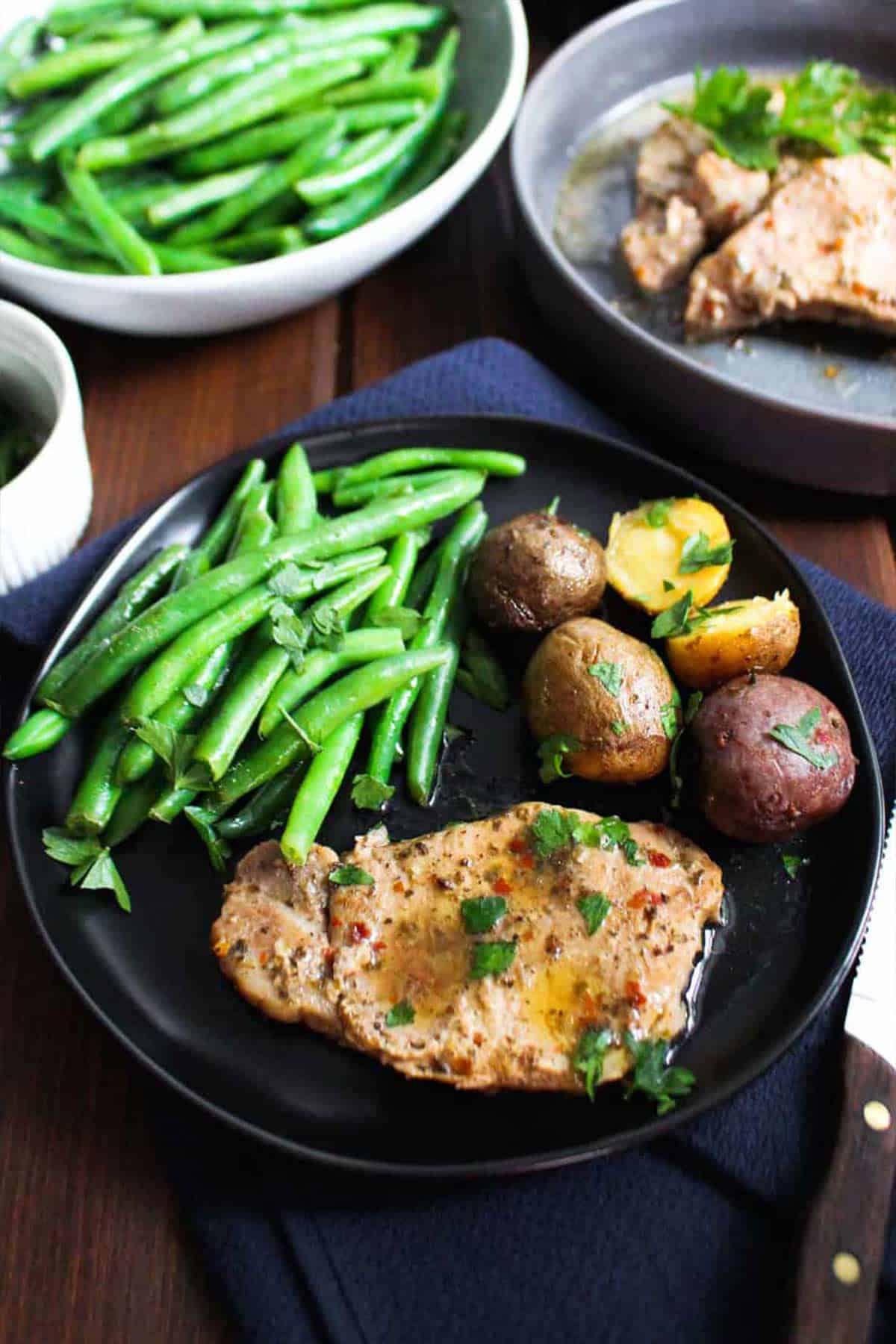 Crock pot pork chops and potatoes on black plate with steamed green beans.