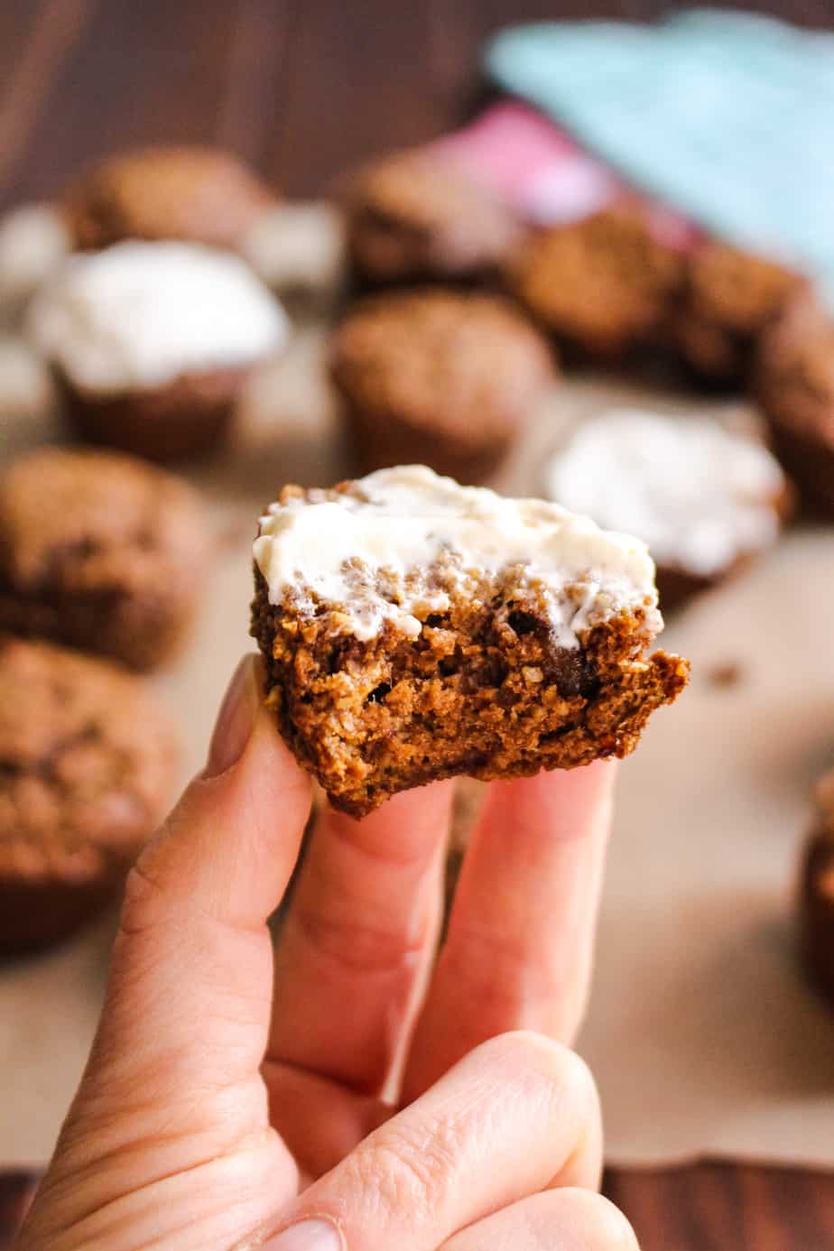 hand holding one gingerbread muffin with cream cheese frosting bit taken out to show texture