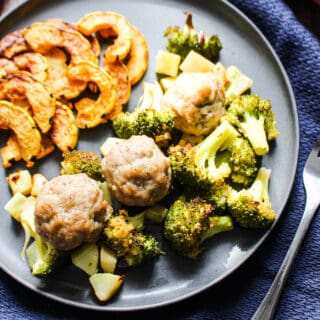 gray slate plate filled with roasted delicata squash, roasted broccoli, and 3 pork sausage meatballs