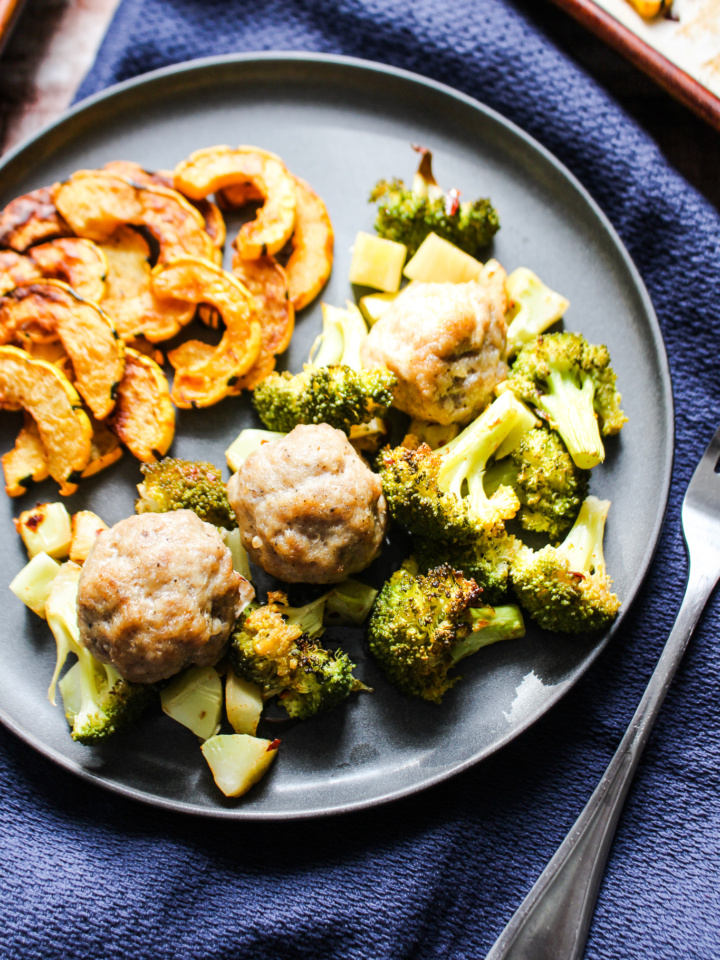 gray slate plate filled with roasted delicata squash, roasted broccoli, and 3 pork sausage meatballs