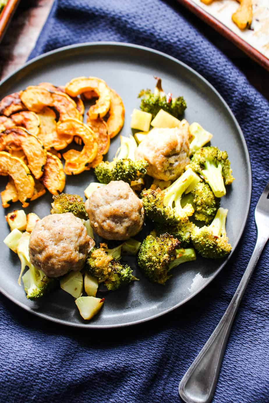 gray slate plate filled with roasted delicata squash, roasted broccoli, and 3 pork sausage meatballs