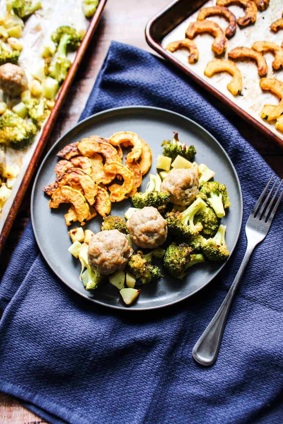 blue napkin with gray plate containing roasted delicata, broccoli, and sausage balls