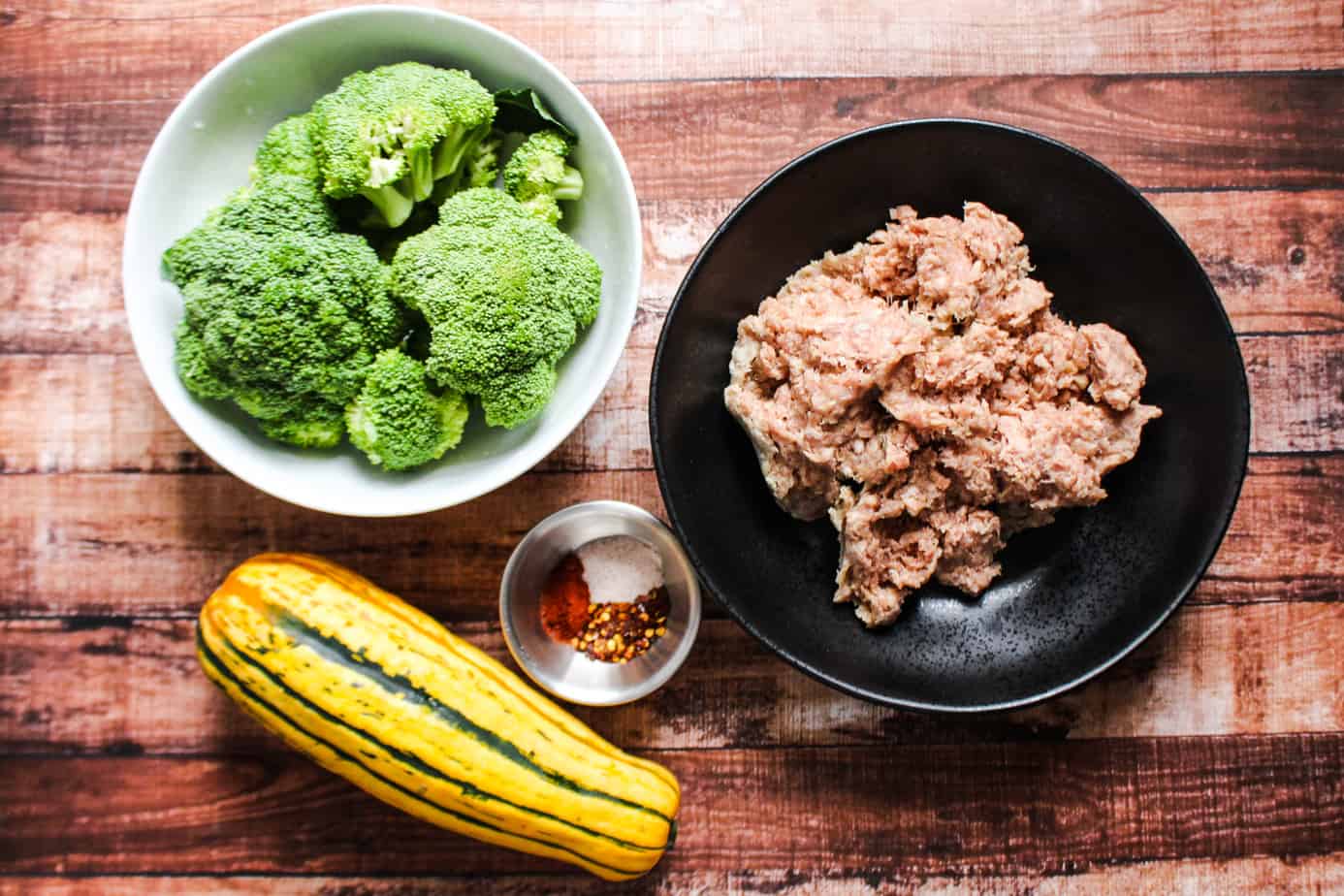 bowl with raw sausage, bowl with broccoli, small bowl with spices, one delicata squash