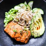 close up of black bowl with salmon, soba, edamame, cucumbers, avocado, black and white sesame seeds