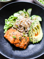 close up of black bowl with salmon, soba, edamame, cucumbers, avocado, black and white sesame seeds