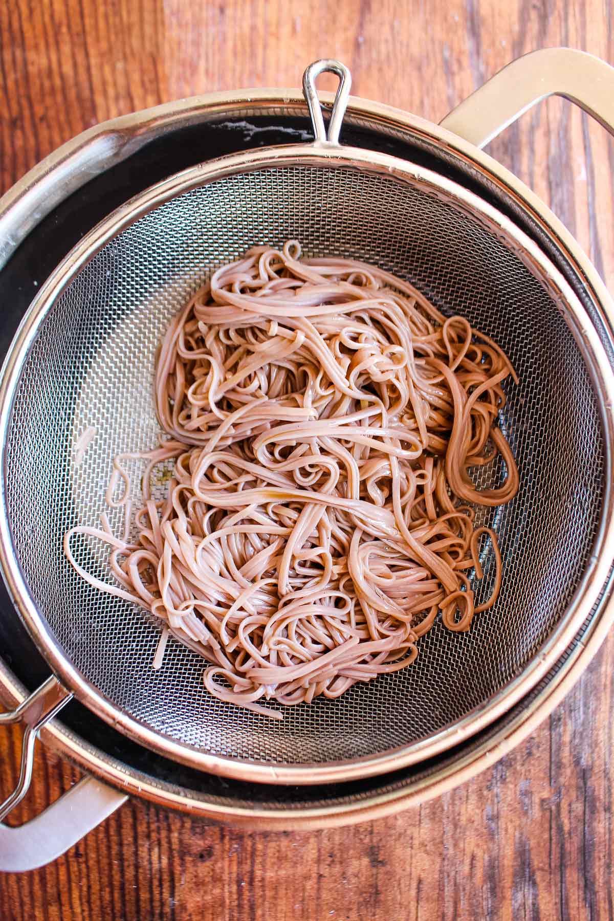 Soba noodles draining in a strainer after cooking.