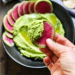 hand holding watermelon into a black bowl with green hummus