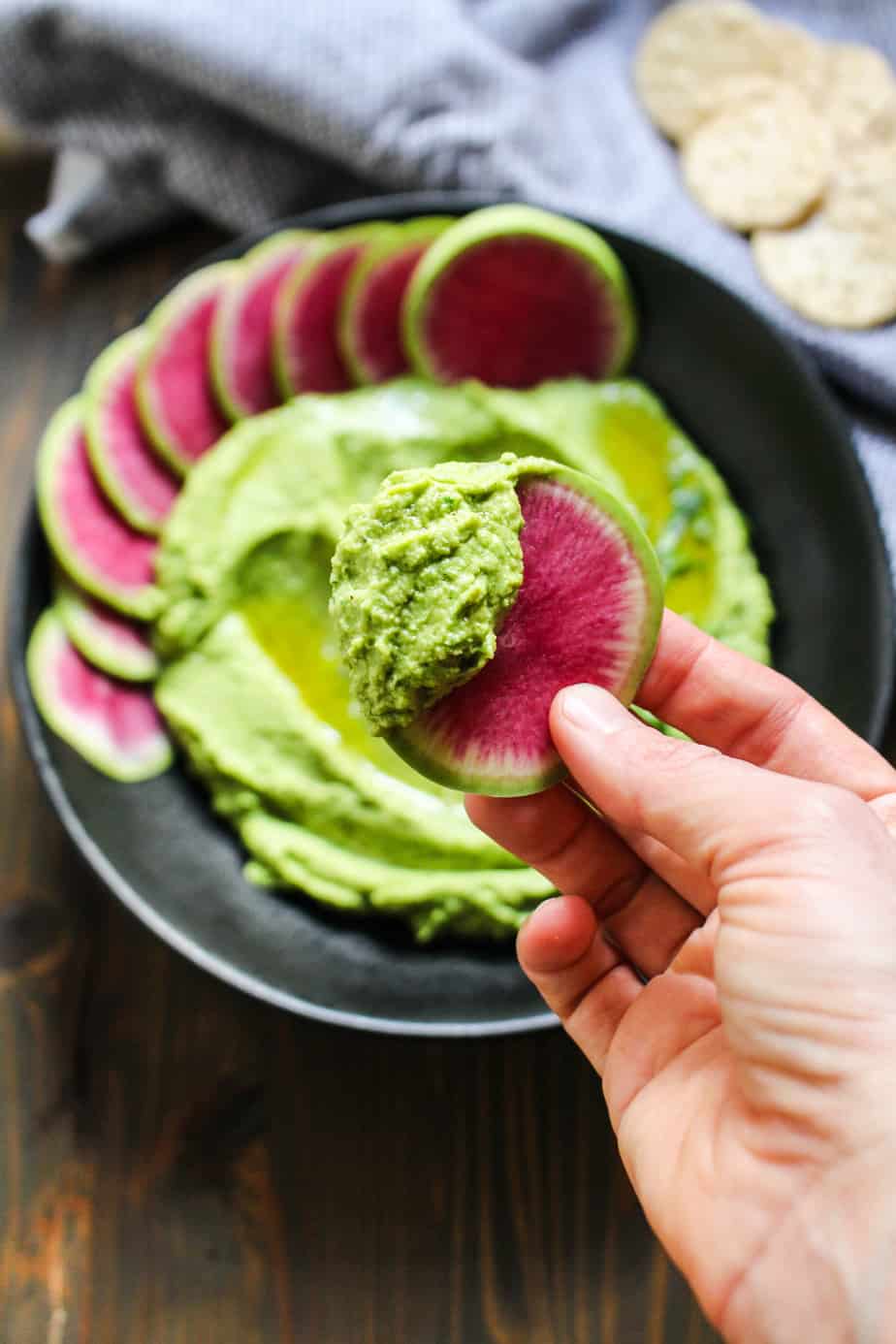 hand holding watermelon into a black bowl with green hummus