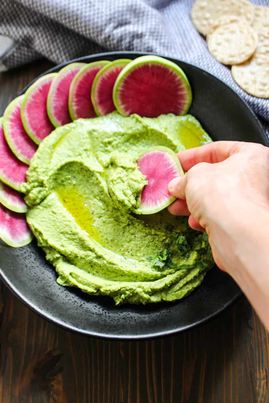 hand dipping watermelon into a black bowl with green hummus