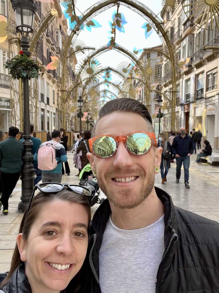 a man and woman standing on a wide shopping street under golden arches in Malaga Centro