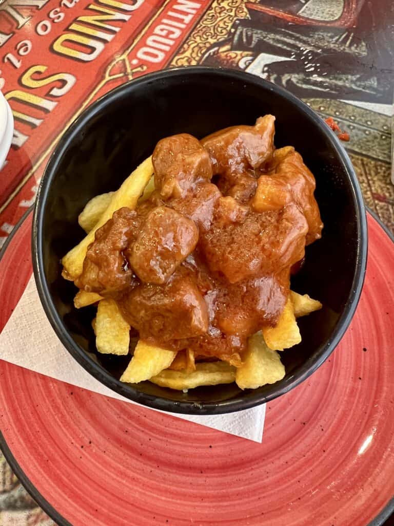 black bowl of fried potatoes topped with chunks of pork slow cooked in tomato sauce