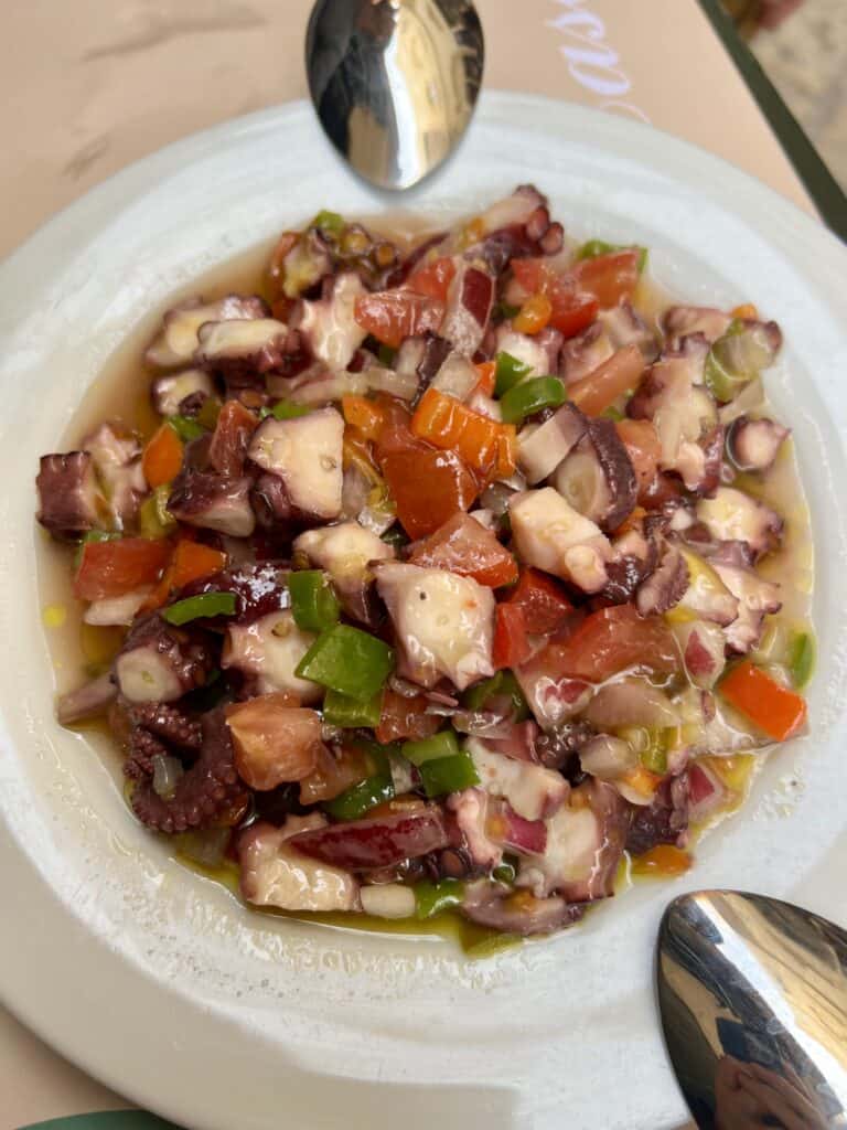 white plate with chopped red and green bell peppers, onions, and cooked octopus in olive oil