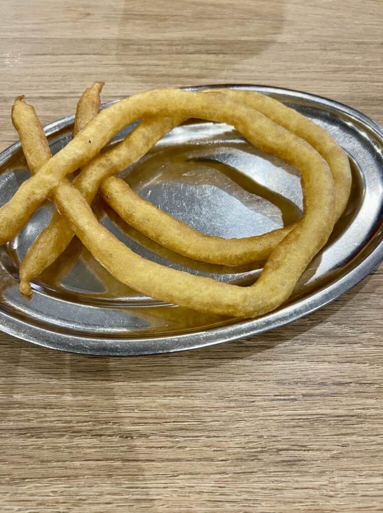 two gluten-free spanish churros on a silver platter