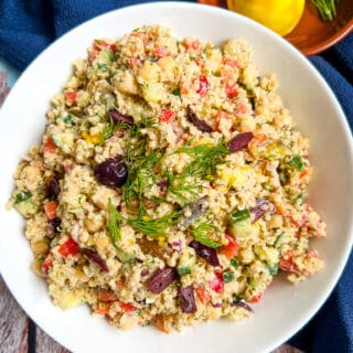 white bowl filled with mixed quinoa tahini salad, topped with fresh dill