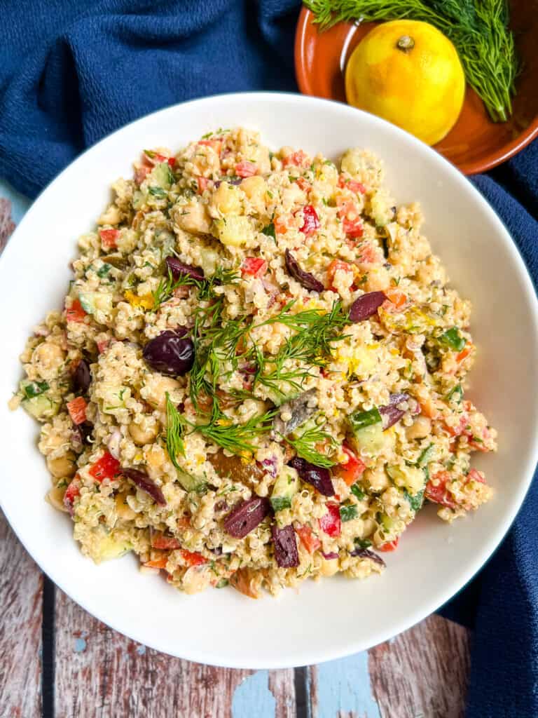 white bowl filled with mixed quinoa tahini salad, topped with fresh dill