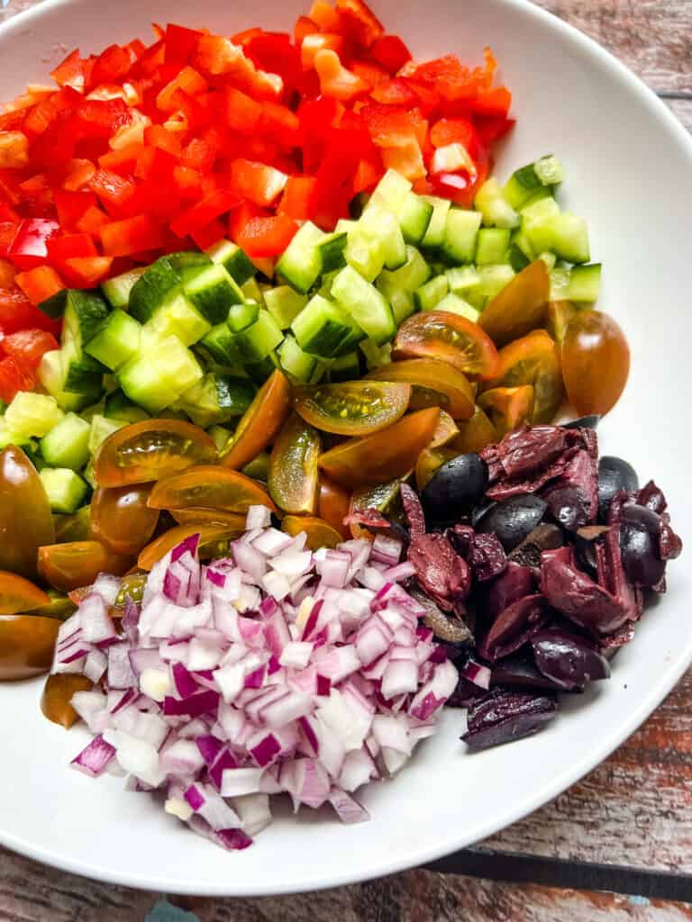 prepped ingredients arranged, chopped red bell pepper, cucumber, tomatoes, red onion, black olives
