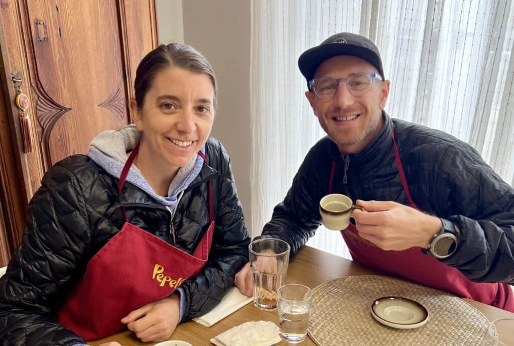 two adults wearing red aprons drinking tea after a Spanish Cooking Class 