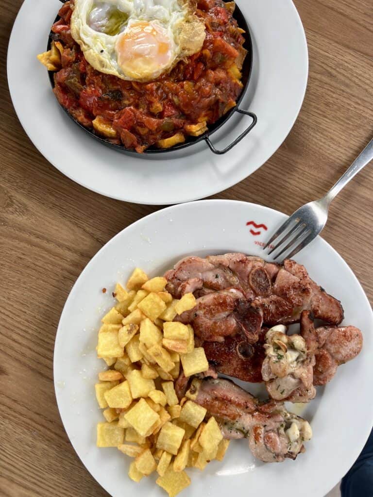 plate of chuletas and fried potatoes and another plate of pisto topped with a fried egg