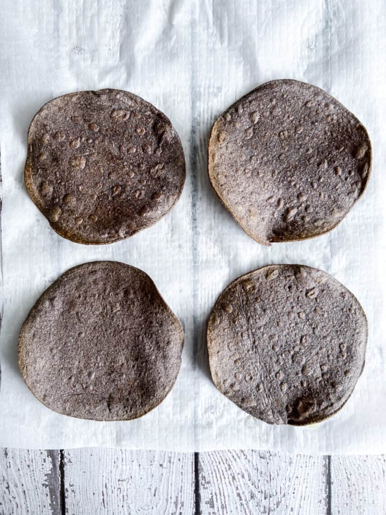 Four crisped blue corn tortillas on parchment paper.