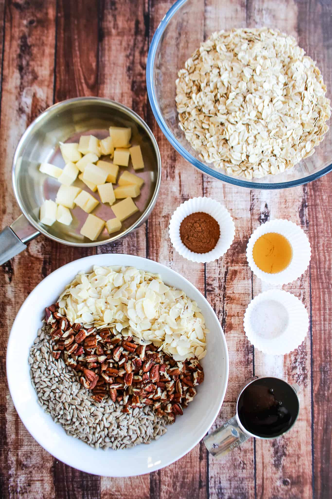 several bowls of best homemade granola ingredients including oats, butter, spices, and various nuts and seeds