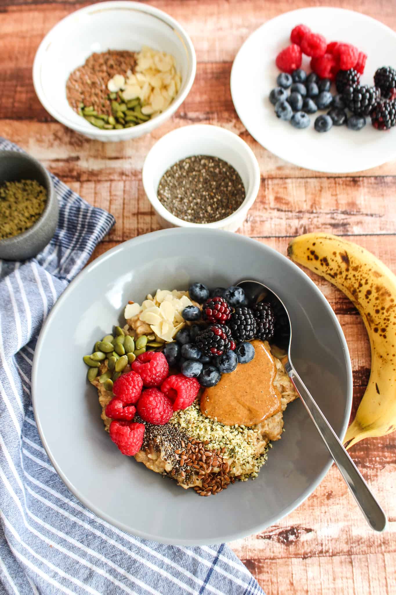 a bowl of mashed banana oatmeal with toppings on it and bowls surrounding it on the table