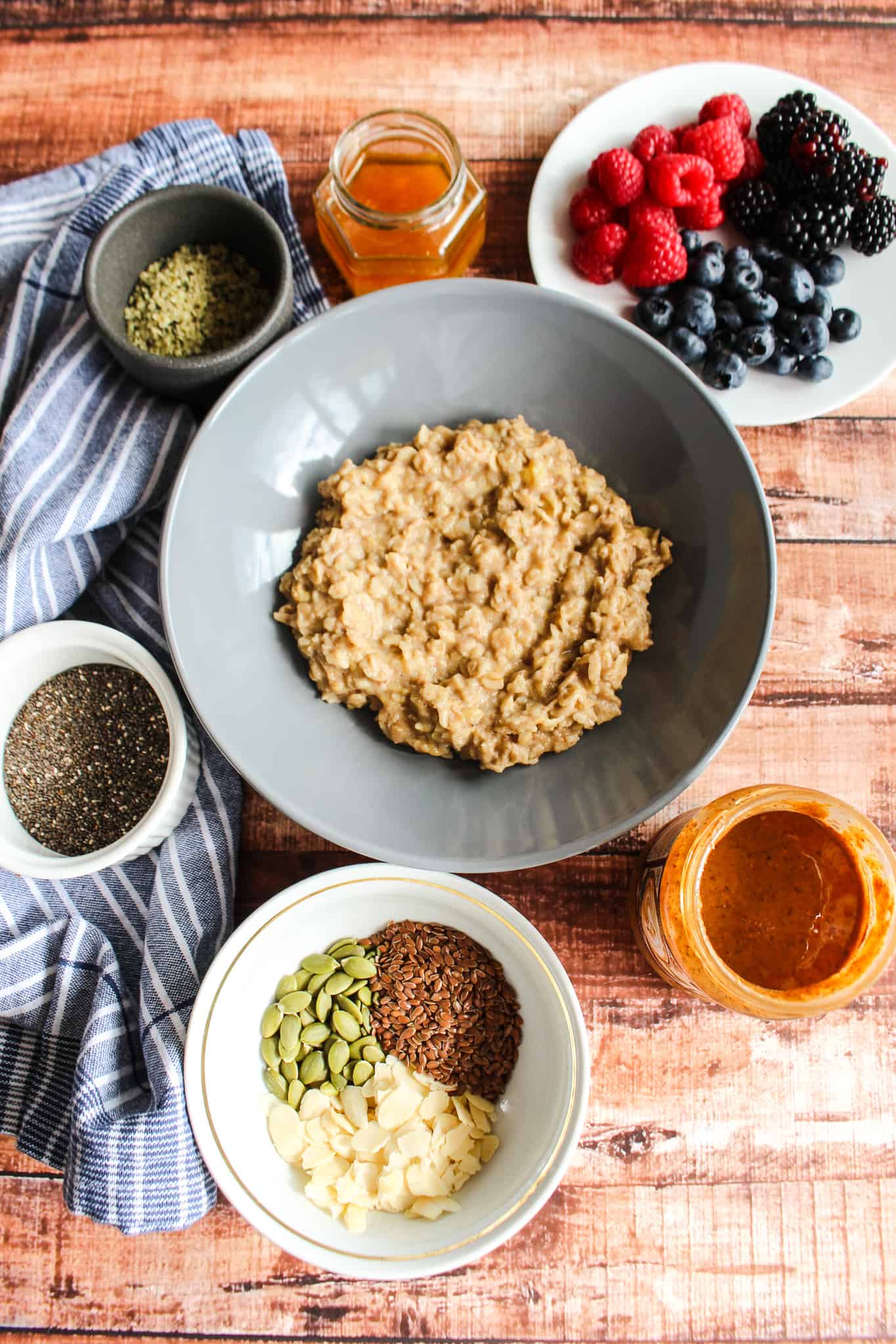 a bowl of mashed banana oatmeal with no toppings surrounded by individual toppings in bowls and cups