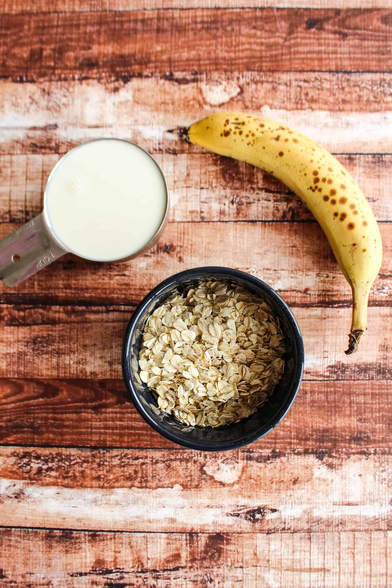 a bowl of uncooked oats beside an unpeeled banana and a cup of milk