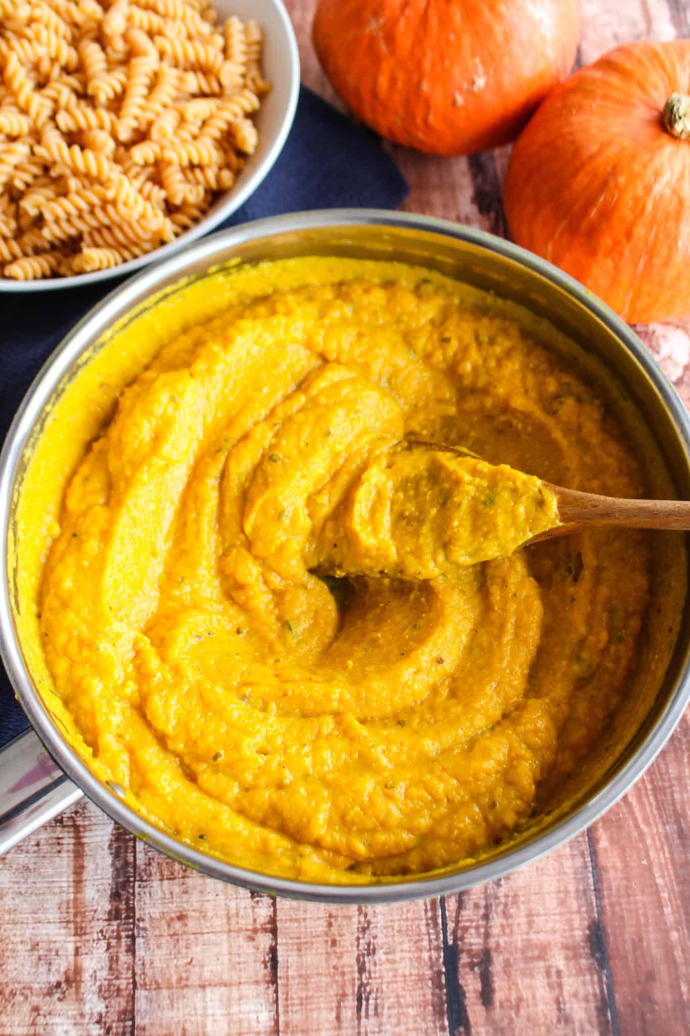 Creamy pumpkin pasta sauce in a bowl beside a bowl of noodles.