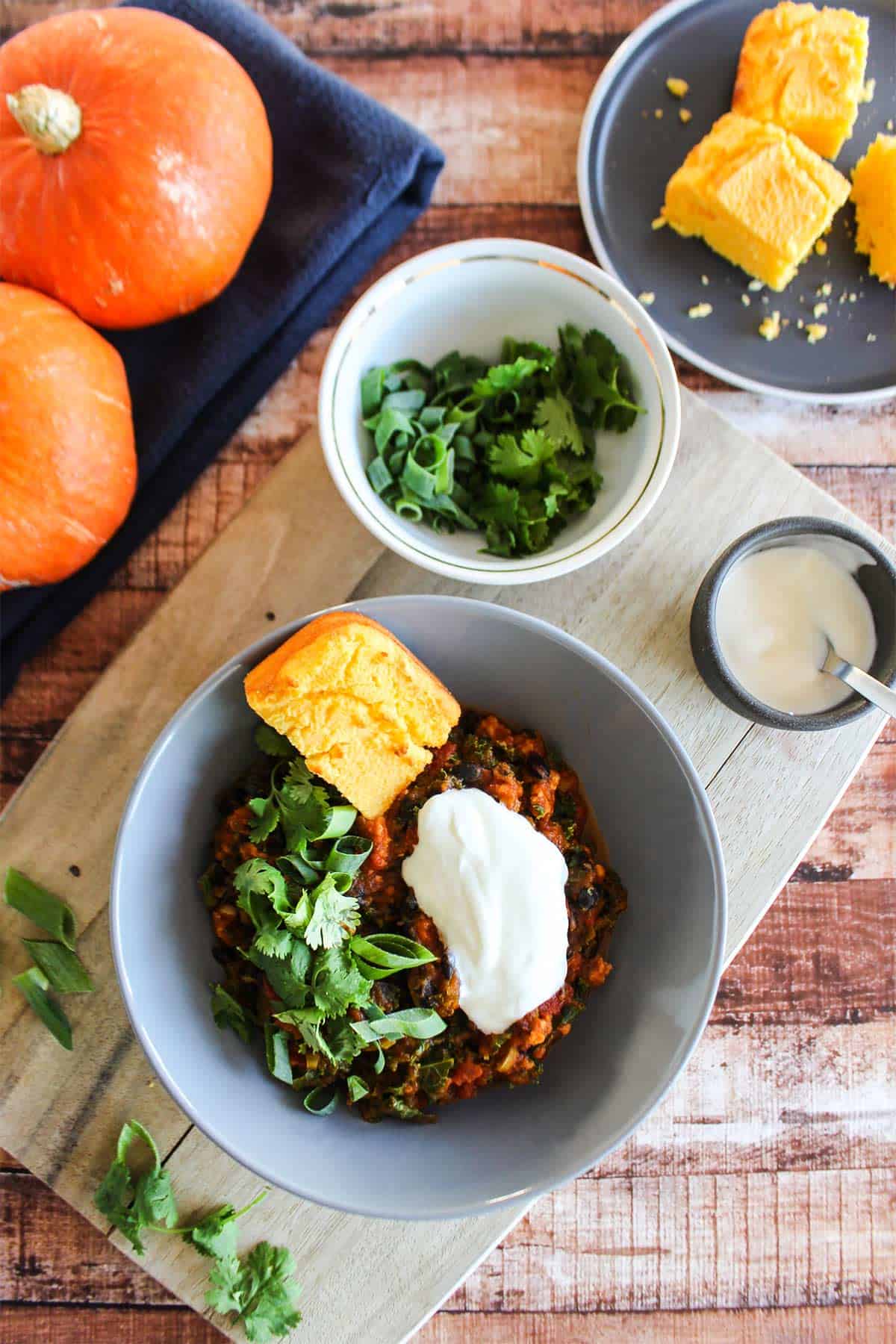 Bowl of pumpkin chili on the table with cornbread and sourcream.