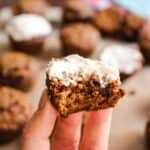 gingerbread oat muffin with maple cream cheese topping being held by fingers with more muffins in the background