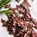 dark chocolate peppermint bark broken into pieces with candy canes and pine beside them