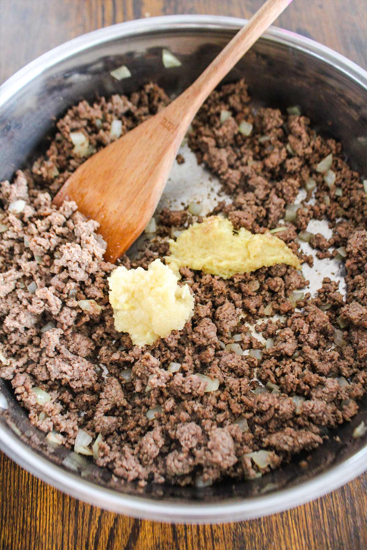 Garlic and ginger added to the onions and beef cooking in the pan.