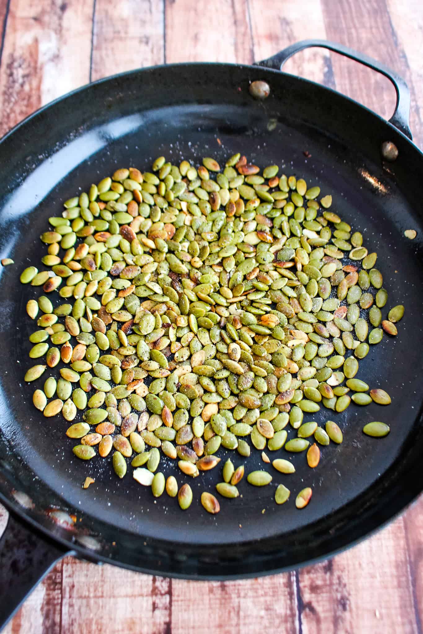 a skillet with pumpkin seeds of various levels of being toasted.