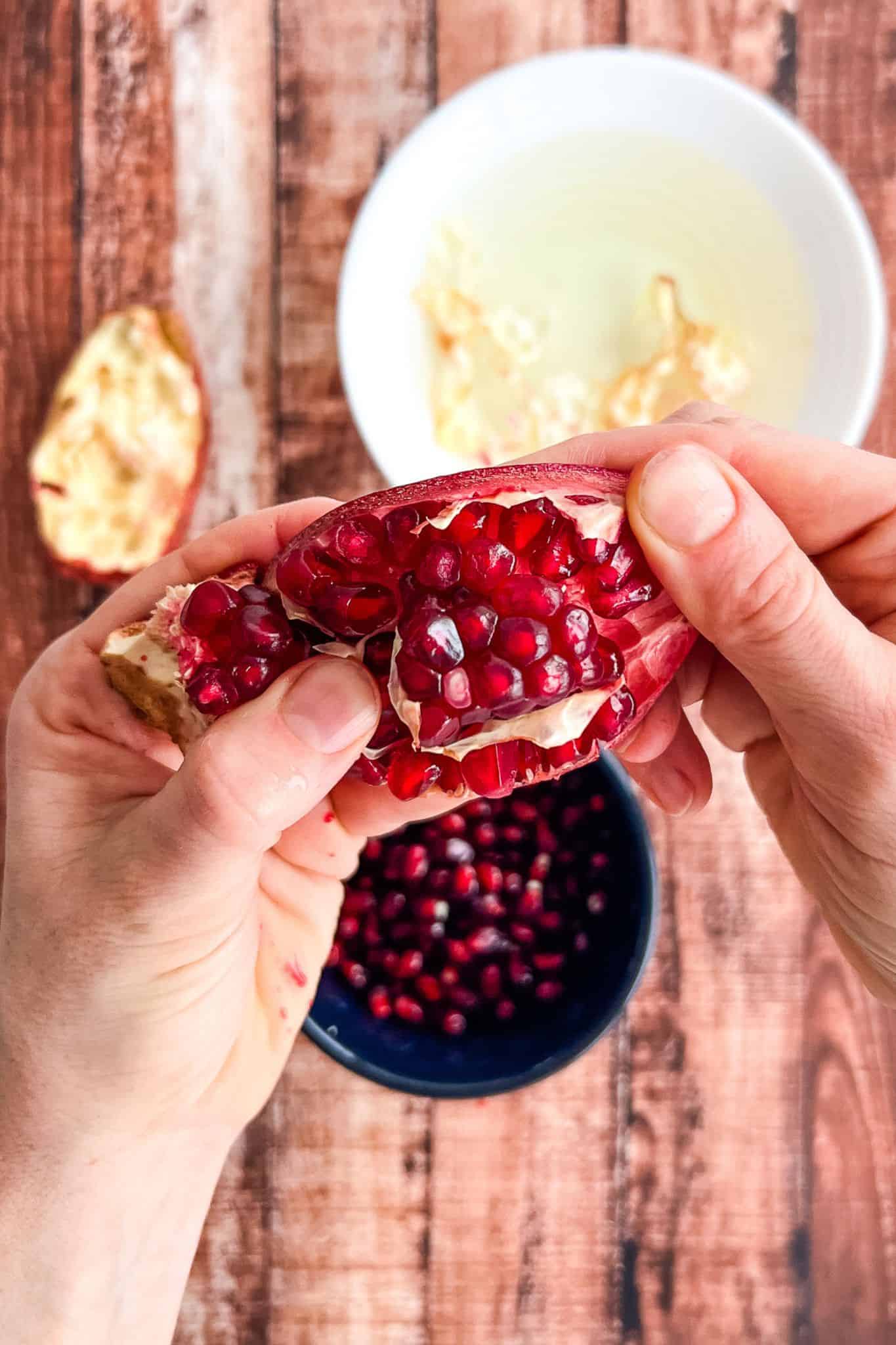 two hands pulling the skin of a pomegranate to release the seeds.