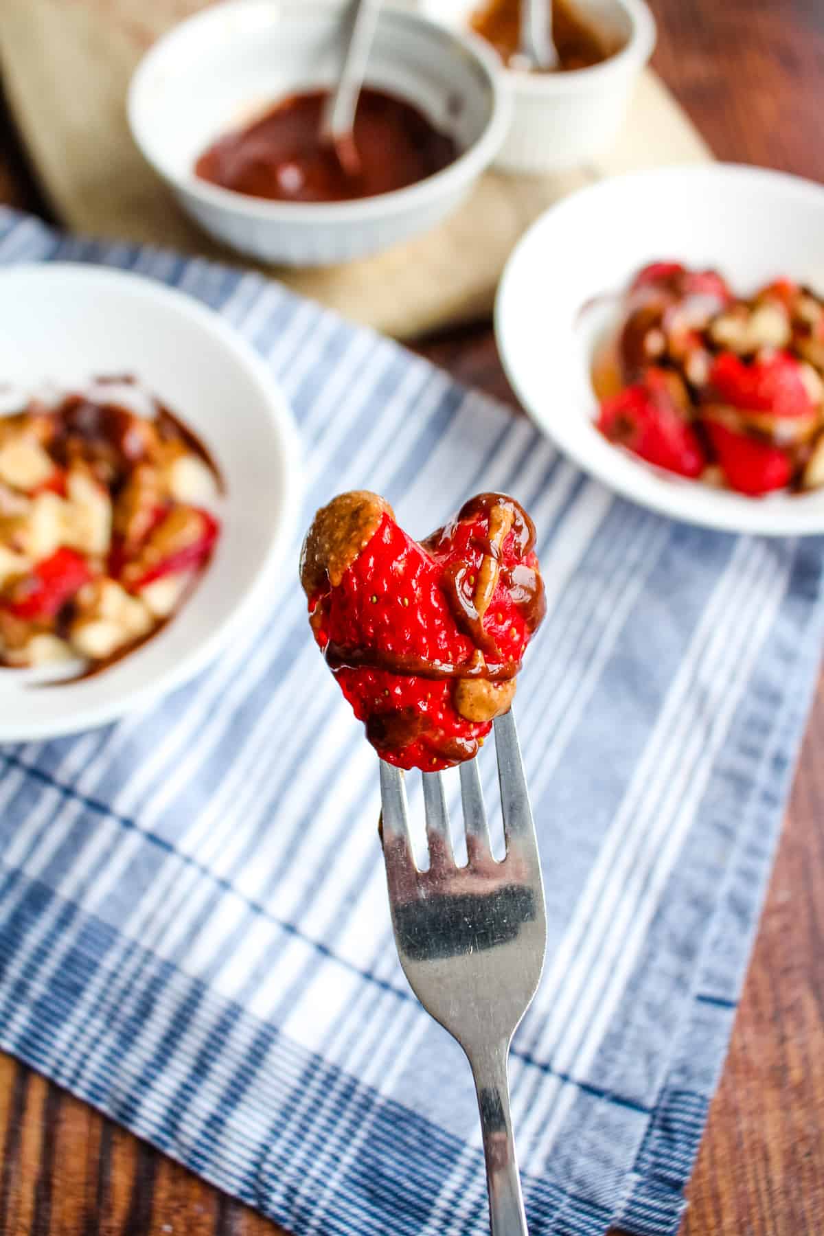 Fork holding a heart-shaped strawberry drizzled with chocolate and nut butter.