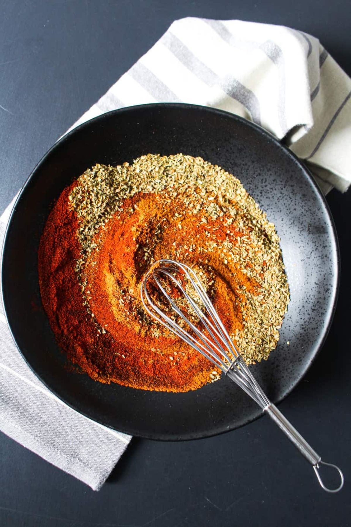 Black bowl with colorful spices being stirred with a whisk.