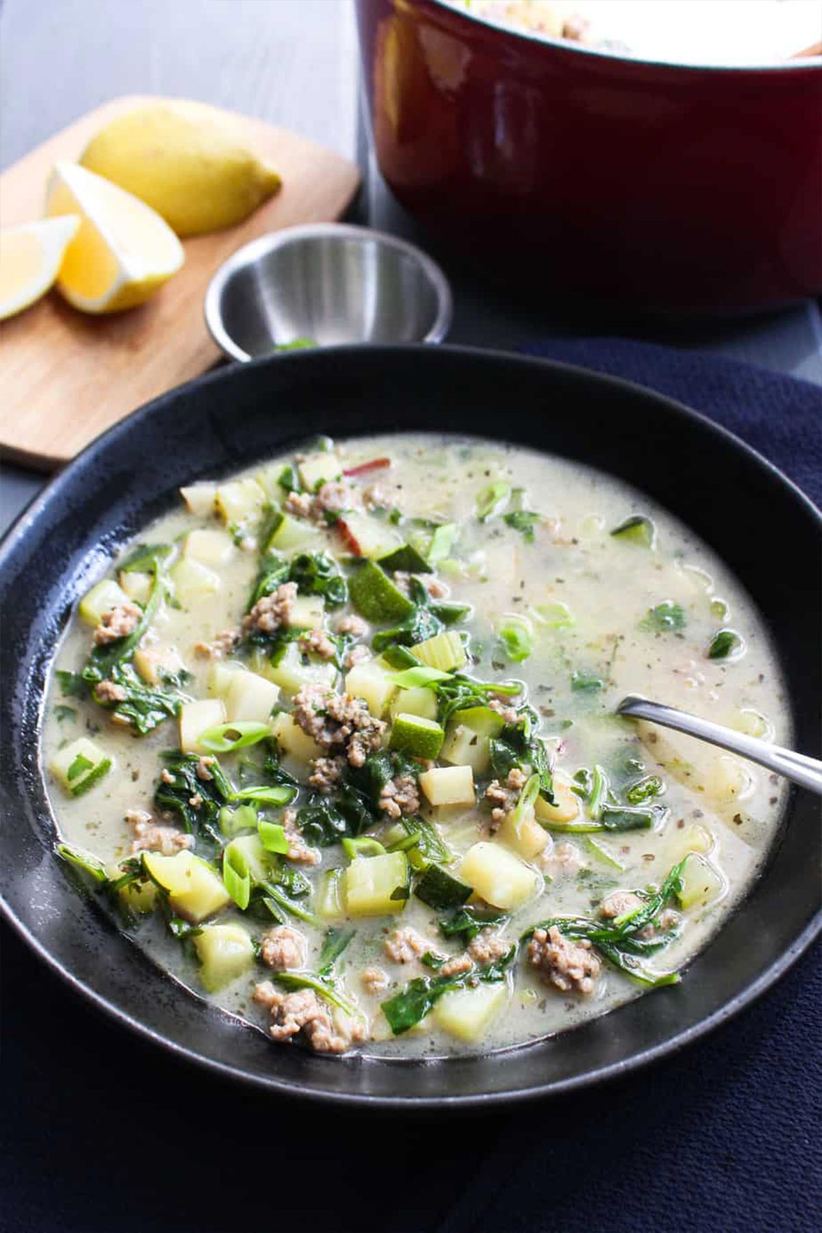 Ground pork soup served up in a black bowl with a spoon in it.