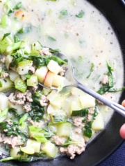 A bowl of ground pork soup with vegetables on the table with a hand easing a soup into the bowl and lifting up a bite.