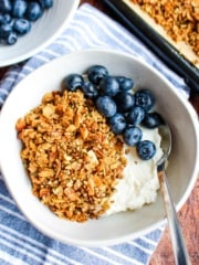 A bowl of vanilla high protein granola on the table with blueberries and yogurt.