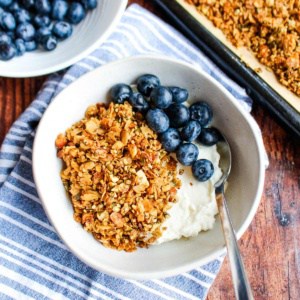 A bowl of vanilla high protein granola on the table with blueberries and yogurt.