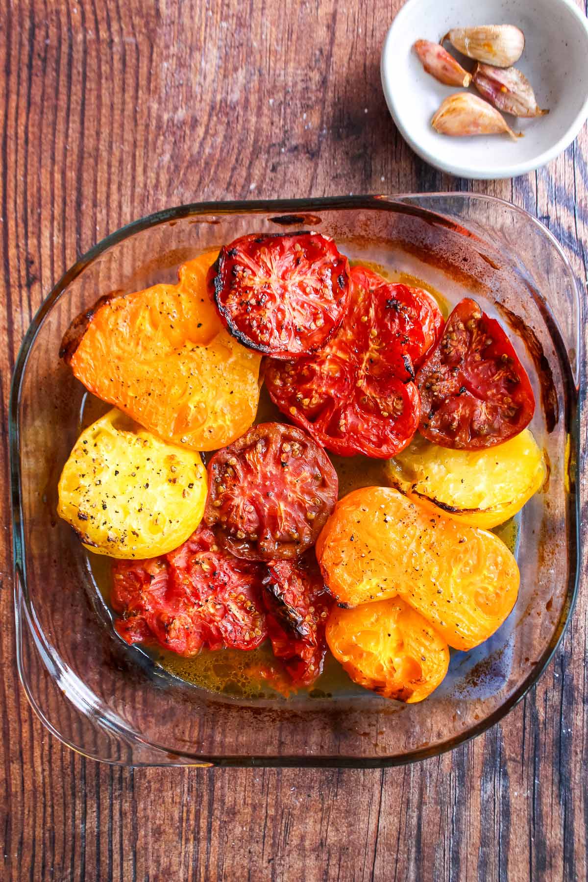 Tomatoes in a baking dish with cloves of garlic.