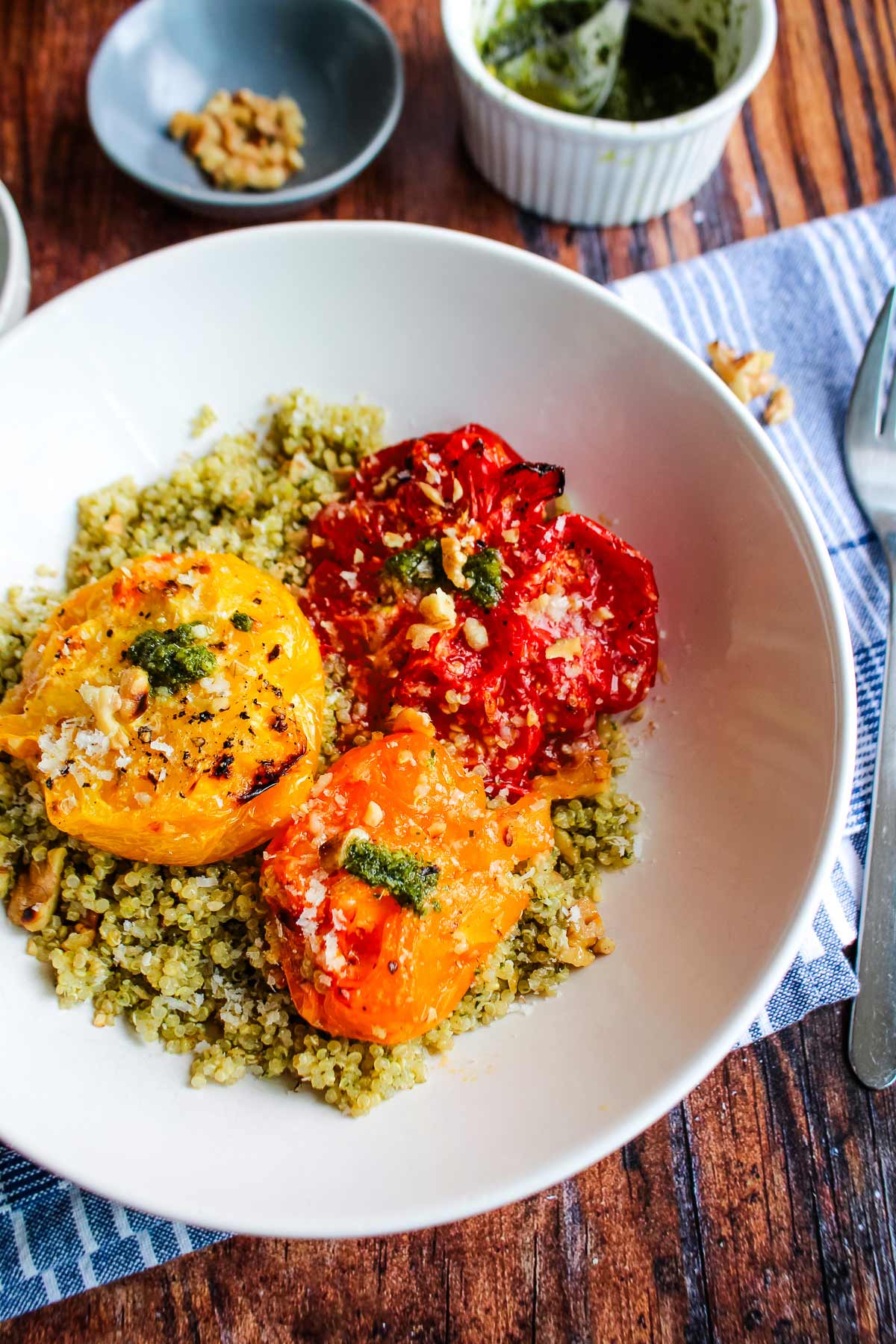 Pesto quinoa in a white bowl with roasted tomatoes on top.