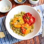 A bowl of pesto quinoa on the table with roasted tomatoes on top.