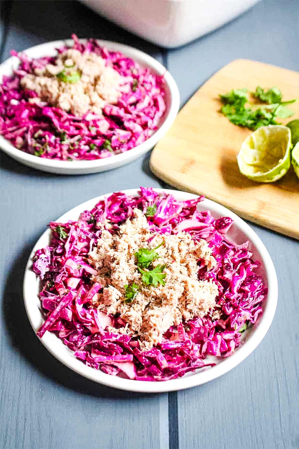 A plate of red cabbage slaw on the table topped with tuna.